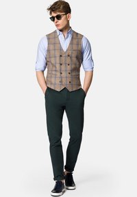 Brązowa kamizelka w kratę na jasnoniebieskiej koszuli, zestawiona z zielonymi spodniami i czarnymi trampkami z białą podeszwą. Całość dopełniają okulary przeciwsłoneczne.