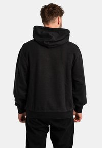 Black hoodie with a spacious hood, ribbed cuffs, and hem. Soft material with a smooth texture, shown from the back on a person.