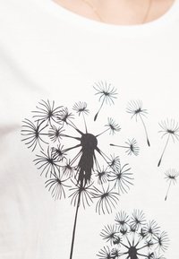 T-shirt en coton blanc avec imprimé de pissenlit noir, présentant des têtes de graines et des tiges détaillées dans diverses tailles et agencements.