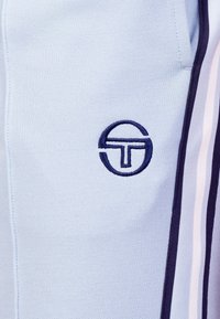 Lichtblauwe poloshirt van textuurstof, met een marineblauw geborduurd logo en witte zijstrepen langs de mouwen.