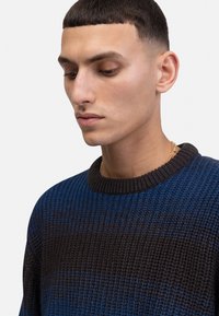 Ronde hals trui met een textuurgebreide ontwerp in afwisselende tinten blauw en bruin. Geribbelde halslijn en subtiele horizontale strepen.
