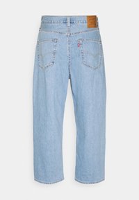 Vaaleansiniset farkut suoran lahkeen muotoilulla, joissa on kaksi takataskua ja ruskea nahkapatchi vyötäröllä.