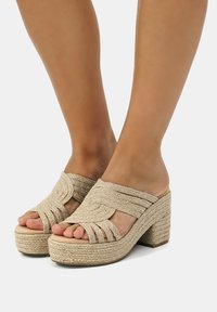 Sandales à plateforme tissées beiges avec un talon bloc haut, dotées de brides croisées et d'un design à bout ouvert. Détail en corde texturée sur la semelle.