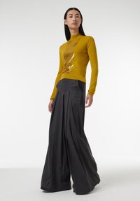 Senfgelbes Sweatshirt mit Pailletten-Details, kombiniert mit hoch taillierten, plissierten dunkelgrauen, weit geschnittenen Hosen. Glatte Texturen, taillierte und fließende Designs.