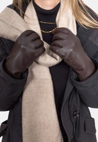 Brown leather gloves with a smooth texture, held tightly around a beige wool scarf, worn with a black coat and a ribbed black top.
