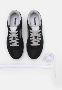 Zwarte suède en mesh sneakers met zilveren accenten, voorzien van grijze veters en een witte zool. Inclusief extra witte veters naast de schoenen.