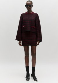 Rood-zwart gemêleerd co-ord set bestaande uit een cropped trui met klokmouwen en een rok, aangevuld met puntige zwarte hakken en sokken.