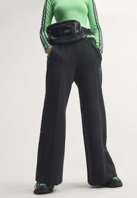 Person wearing black wide-leg pants, green long-sleeve top with black stripes, black sneakers, and a black waist bag.