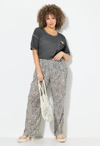 Grijze T-shirt met korte mouwen, zwarte en witte patroon broek in relaxed-fit, crèmekleurige platform sandalen en een geweven crèmekleurige tas.