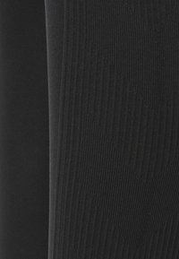 Svarta ribbade leggings i tyg, med en texturerad design med vertikala linjer, slät yta och en åtsittande form.