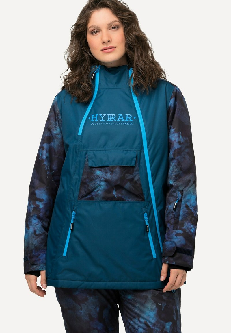 Giacca esterna color teal con colletto alto, accenti blu e maniche con pattern astratto blu scuro. Presenta una tasca frontale e tasche laterali con zip.