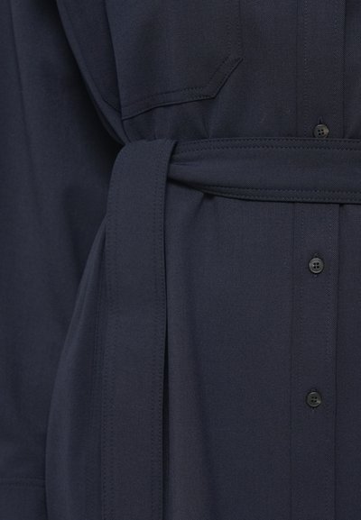 Ναυτικό μπλε πουκάμισο με μαλακή υφή, διαθέτει κλείσιμο με κουμπιά στο μπροστινό μέρος, δύο τσέπες στο στήθος και ζωνάκι από ύφασμα στη μέση.