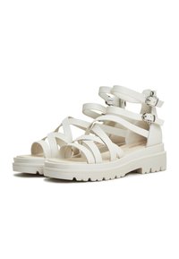 White strappy sandals with wide straps, open toes, and adjustable ankle buckles. Chunky soles with a textured, rugged bottom.