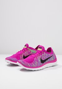 Běžecké boty Nike s živým růžovým pleteným svrškem, černým swishem, limetkově zelenými akcenty a lehkou bílou podrážkou se strukturovaným designem.