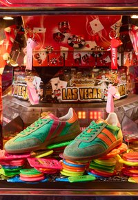 Des baskets vertes et orange affichées sur des jetons de casino colorés à l'intérieur d'une machine à griffes sur le thème de Las Vegas.