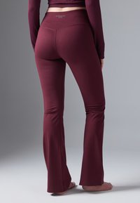 Bordowe legginsy w stylu dzwonów z gładką fakturą i elastycznym paskiem w talii, z logo marki z tyłu oraz dopasowanym krojem.