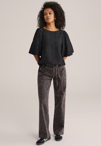 Top de manga abullonada texturizada negra combinado con pantalones marrones estampados, que cuentan con una cintura con cordón y zapatillas negras. Diseño simple y moderno.