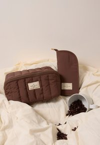 Trousse de maquillage en tissu matelassé marron et pochette fine, toutes deux avec des étiquettes en tissu. Présente une fermeture éclair lisse et un motif texturé sur la surface.