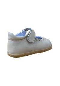 Zapato Mary Jane de cuero beige con puntera redonda, correa ajustable de Velcro y detalles perforados en la parte superior. Suela de goma visible.