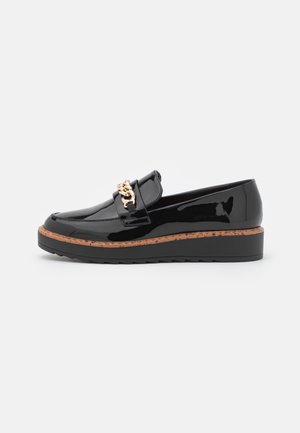 Mocassin noir verni avec semelle à bordure marron et détail chaîne dorée sur le dessus, semelle plateforme plate, vue de côté sur fond blanc.