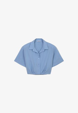 Camicia corta di colore azzurro chiaro con maniche corte, bottoni frontali, colletto e strisce verticali testurizzate. Presenta un dettaglio in vita arricciato.