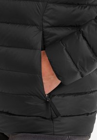 Black puffer jacket with segmented padding, zippered pockets, and a snug cuff. The fabric appears shiny and has a smooth texture.