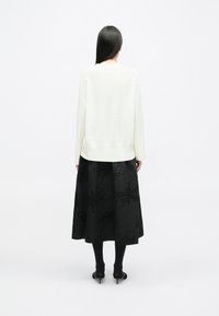 White knitted sweater, black floor-length skirt with textured embroidered patterns, worn with black tights and pointed heels.