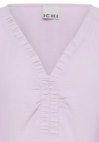 Chemise violet clair à col en V avec volant vertical sur l'encolure et le centre devant, affichant l'étiquette de la marque "ICHI" à l'intérieur du col.