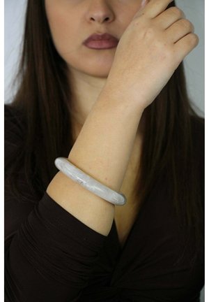 Transluzentes graues Armreif-Armband, das am Handgelenk getragen wird und eine glatte, polierte Oberfläche sowie eine leicht trübe Textur aufweist.