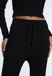 Svart ribbat stickat lounge-set som består av en kort topp och byxor med dragsko i midjan och textilier med struktur.