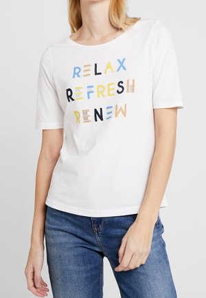 Kobieta w białej koszulce z krótkim rękawem z napisem „RELAX REFRESH RENEW” wielobarwnymi literami, w połączeniu z niebieskimi dżinsami.