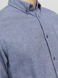 Camisa de vestir azul con patrón de espiga, que presenta un cuello clásico, un bolsillo en el pecho y botones oscuros. Fabricada con una tela texturada.