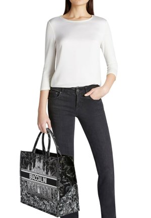 Borsa tote con motivo in bianco e nero con la scritta "BRACCIALINI", abbinata a una maglia a maniche lunghe bianca e jeans neri. La borsa è dotata di doppi manici.