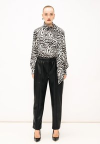 Zwart-wit gestreepte blouse met een strikje, gecombineerd met zwarte neplederen broek en zwarte puntige hakken. Glad stoftextuur.