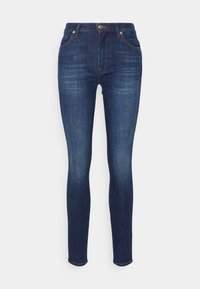 Jeans ajustados en denim oscuro. Cuenta con cierre de cremallera, botón y diseño de cinco bolsillos. Textura ligeramente desgastada en la parte frontal.