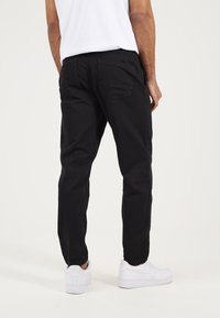 Pantalones de algodón negros con un corte relajado, dos bolsillos traseros y detalles de costura, combinados con zapatillas blancas.