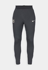 Pantaloni sportivi grigi realizzati in tessuto a coste con un design aderente. Presentano un logo Nike e un crest dell'FC Barcelona sulla gamba sinistra.