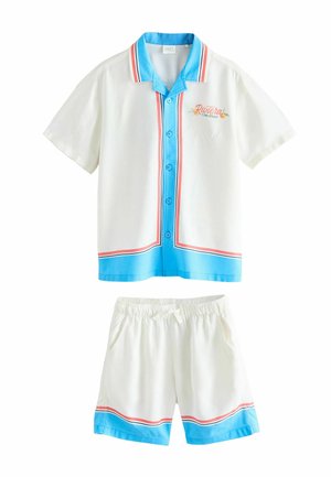 Biały zestaw koszula z krótkim rękawem na guziki i szorty z niebiesko-czerwonym wykończeniem, tekst "Riviera Côte d'Azur" na piersi koszuli.