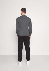 Gray knit sweater with a round neck, ribbed cuffs, and hem, paired with black elastic waist pants and white sneakers, viewed from behind.