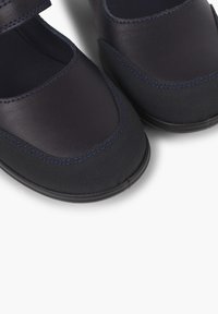 Pantofi bleumarin dintr-o combinație de piele netedă și țesătură texturată, cu vârf rotunjit și o curea cu arici pentru o ajustare ușoară.