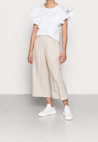 Top blanco con mangas acampanadas combinado con pantalones de pierna ancha beige y zapatillas blancas. Textura suave, corte relajado y paleta de colores neutros.