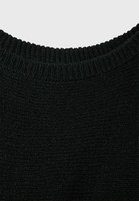 Gros plan d'un col de pull noir tricoté avec une texture côtelée sur un fond clair.