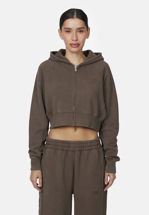 Felpa corta marrone con zip frontale, cappuccio con cordino e polsini a coste. Abbinata a pantaloni della tuta coordinati con vita elasticizzata.