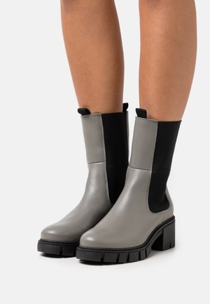 Bottines en cuir gris avec des panneaux latéraux élastiques noirs, semelles épaisses noires et finition lisse, mettant en avant un design moderne.