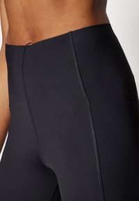 High-waisted black leggings made of smooth, stretchy fabric with visible stitching and a side pocket detail.
