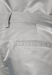 Grå vävd tygbyxa med en slät yta, en bakficka och ett midjeband med en ögla för justering eller fäste.