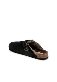 Svarta mockasiner med konstpälsfoder, korkfotbädd och en sidoknappsdetalj. Stilren, slip-on-design med en texturerad gummisula.