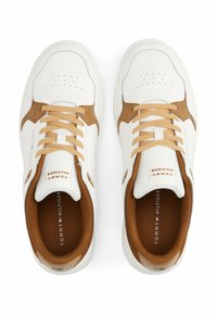 Baskets blanches avec des accents en daim beige, lacets texturés et détails du logo sur la languette. Perforations sur la zone des orteils pour la respirabilité.