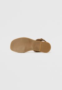 Bruna mockaskor med en platt gummisula. Har en justerbar rem och ribbad textur på sulan för bättre grepp.