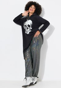 Felpa nera con grafica di un teschio, design asimmetrico, abbinata a pantaloni lucidi e iridescenti. Stivaletti argento alla caviglia completano il look.